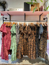 Clothing rack with various dresses hanging on it, with a shelf above containing a fan and speakers.