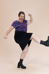 Woman in a black skirt and purple top posing on a beige background